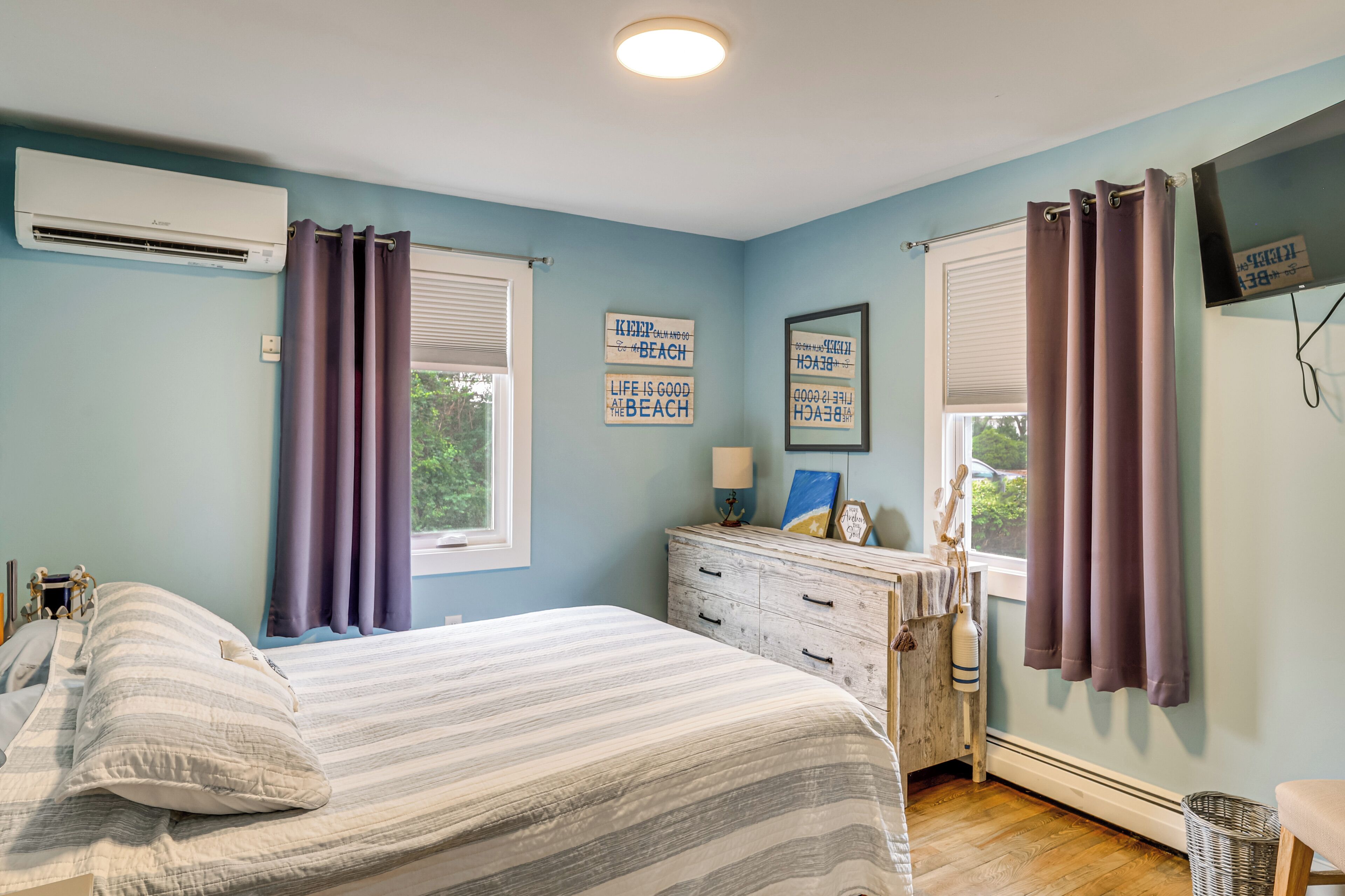 A bedroom with a bed, a dresser, a television, and a window with curtains.