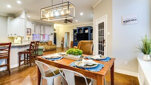 A dining area with a wooden table set for four, surrounded by white chairs. A chandelier hangs above, and a ceiling fan is visible. - Group-friendly Burleson Getaway w/ Outdoor Oasis (Burleson)