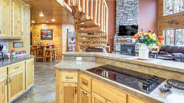 A wooden cabin interior with a kitchen featuring a central island, a stone fireplace, and a spiral staircase. - Big Pine Lake Home w/ Dock & Game Room in Aitkin (Aitkin)