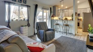 A modern living room with a grey sofa, a ceiling fan, and a view of the kitchen. - Lake Ozarks Home w/ Deck, Dock & Hot Tub (Versailles)
