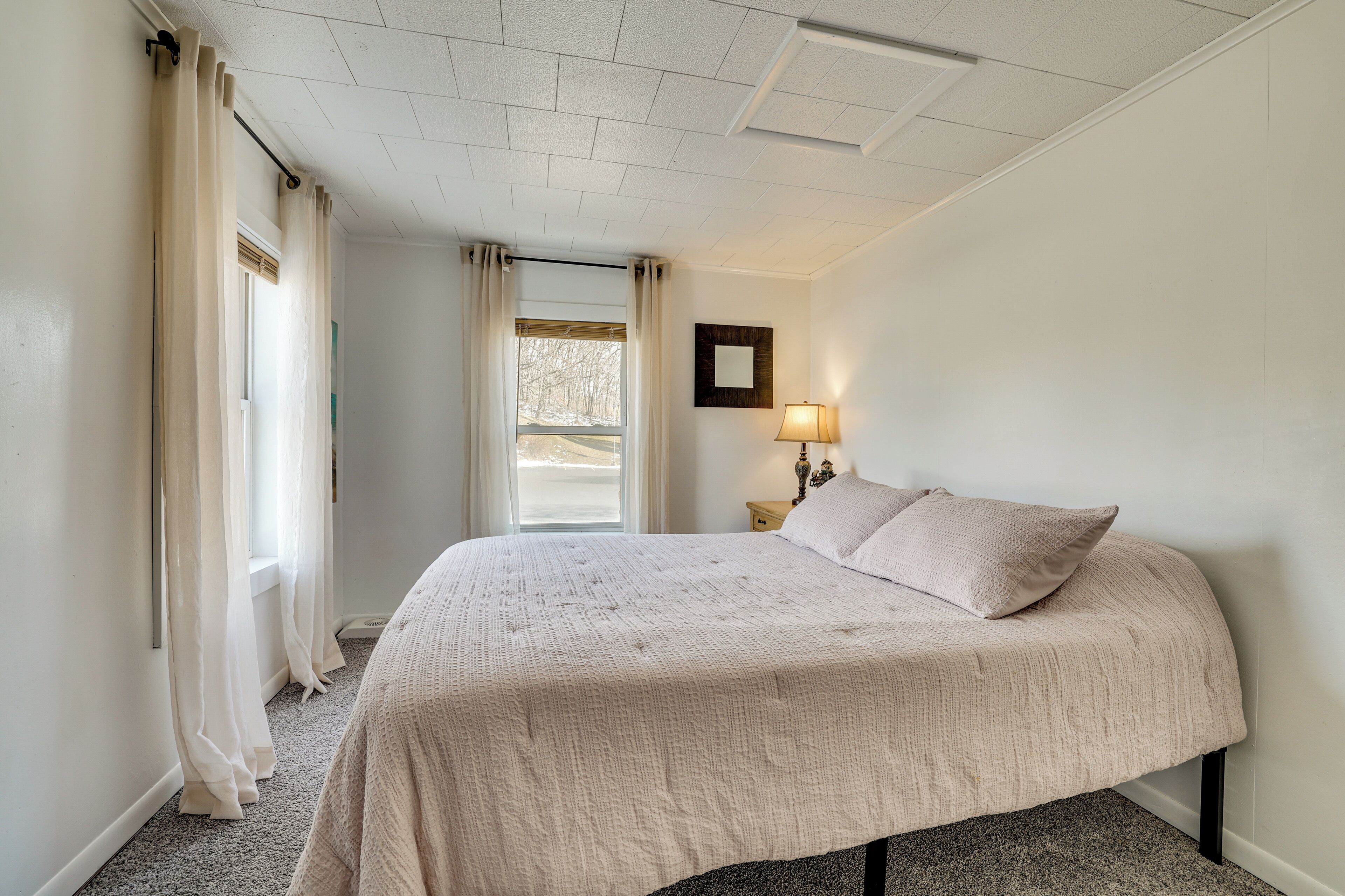 A bedroom with a bed, a nightstand, a lamp, and a window with curtains.