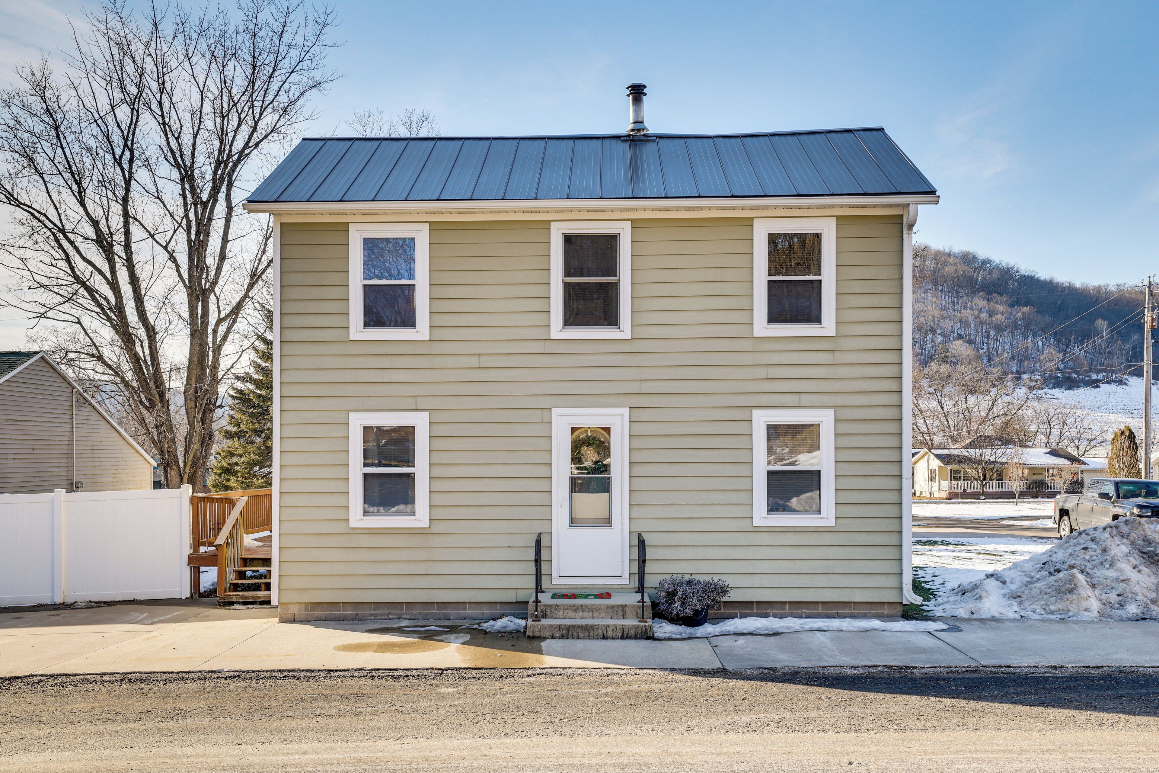 A two-story house with a metal roof, a front porch, and a small garden area.
