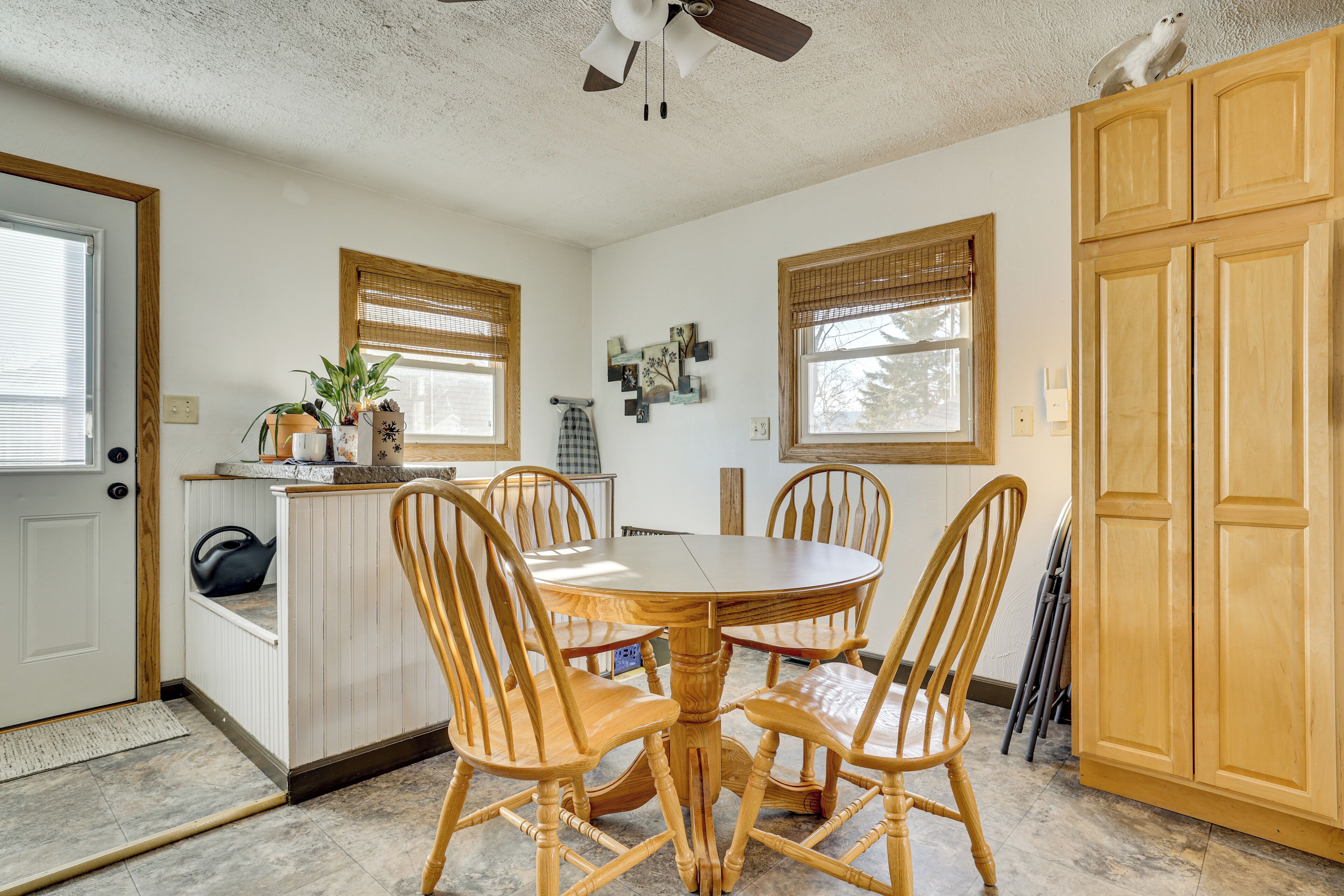 A dining area with a round wooden table and four chairs, a ceiling fan, and wooden cabinets.