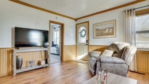 Un salon avec un téléviseur posé sur une console en bois, un canapé en cuir et une table à manger agrémentée d’un vase et d’un vélo.