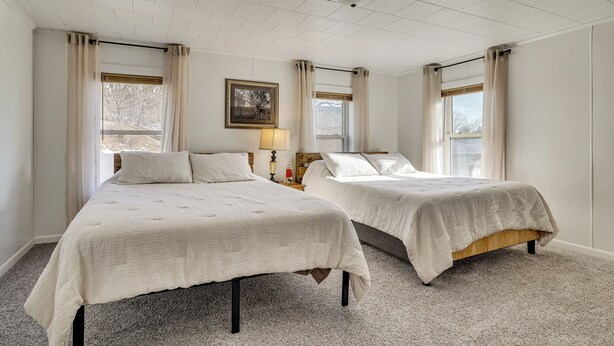 Une chambre d’hôtel avec deux lits, un luminaire au plafond, un tableau encadré au mur et une fenêtre avec des rideaux.