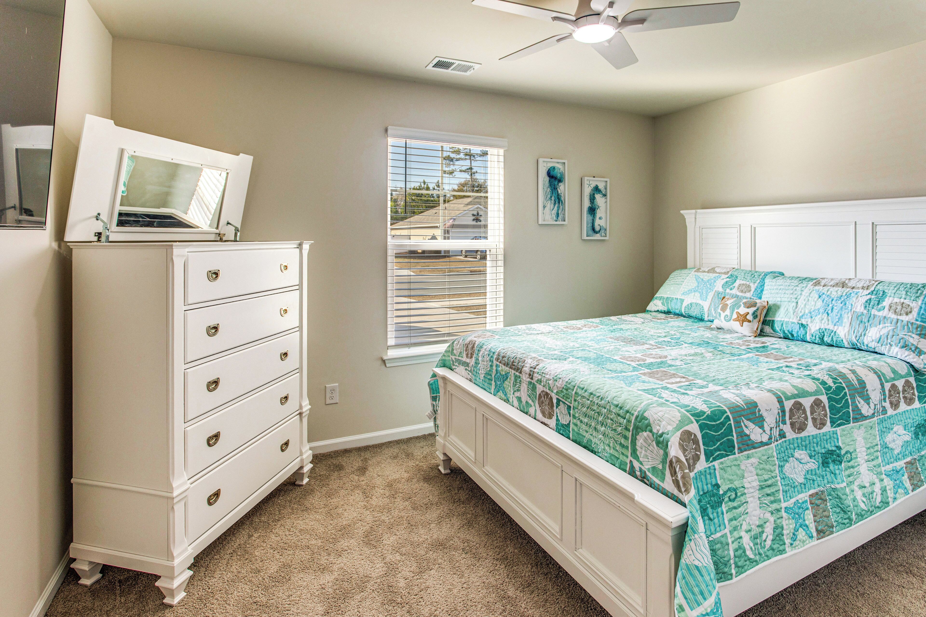 A bedroom with a bed, dresser, and a window with blinds.