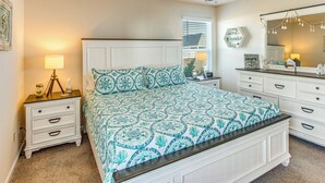 A bedroom with a large bed, a nightstand with a lamp, a dresser, and a mirror. - 3 Mi to Holden Beach! Family Home w/ Patio (Supply)