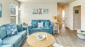 A living room with a blue sofa, a round coffee table, and a wall with nautical-themed artwork. - 3 Mi to Holden Beach! Family Home w/ Patio (Supply)