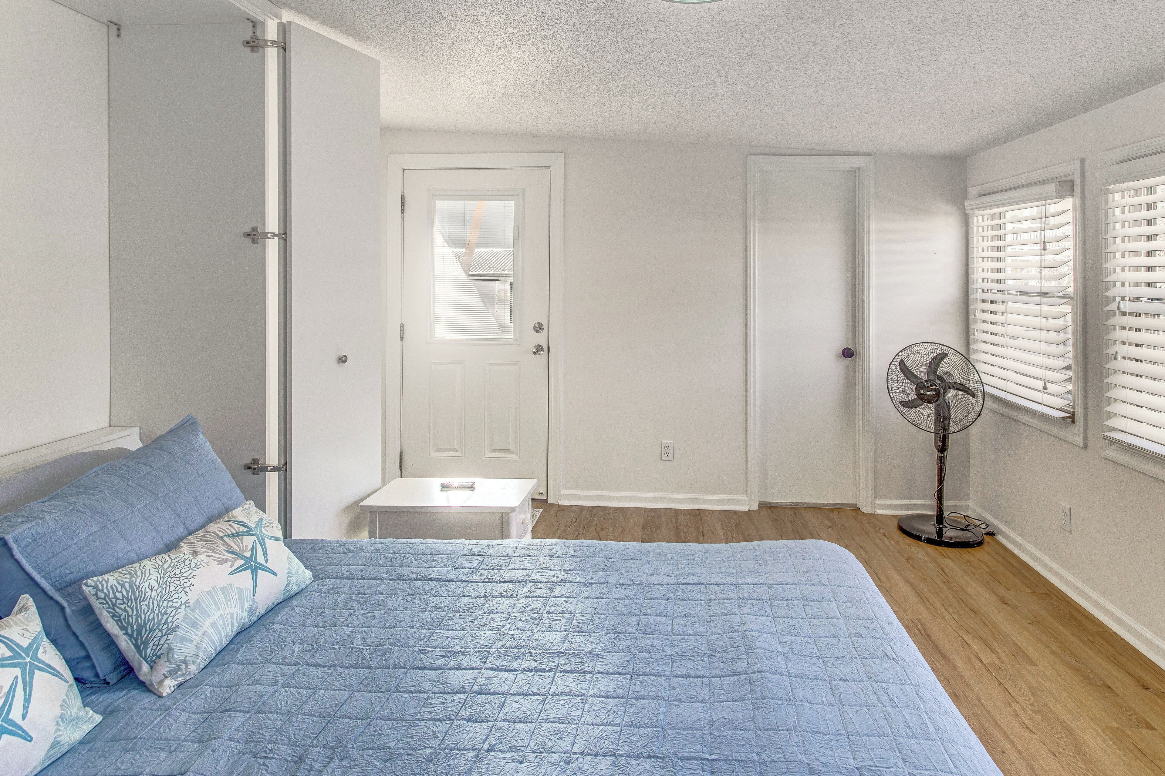 A bedroom with a bed, a nightstand, a fan, and a door leading to a closet.