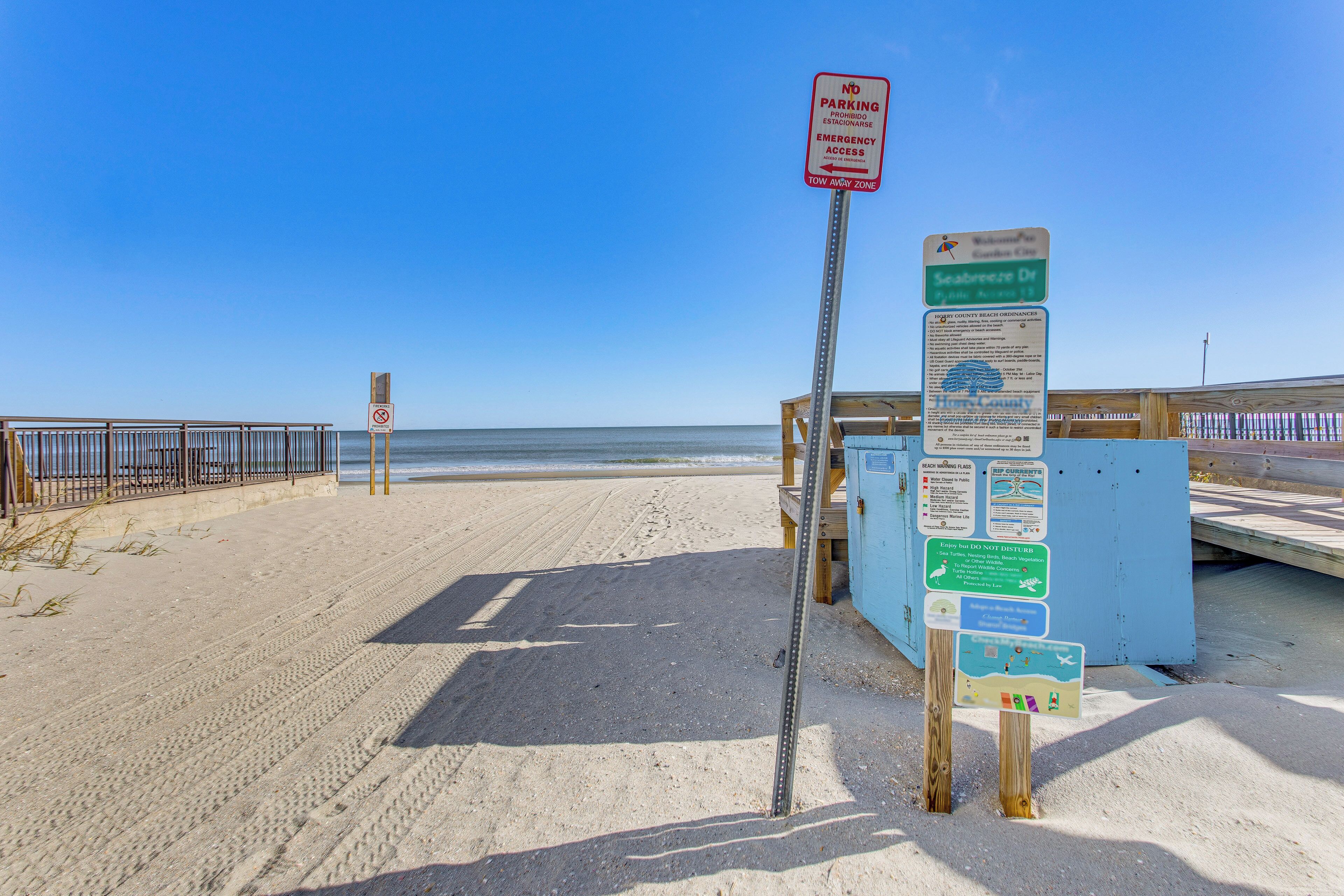 Een strand met een parkeerverbodsbord, een houten looppad en informatieborden over strandregels en lokale bezienswaardigheden.