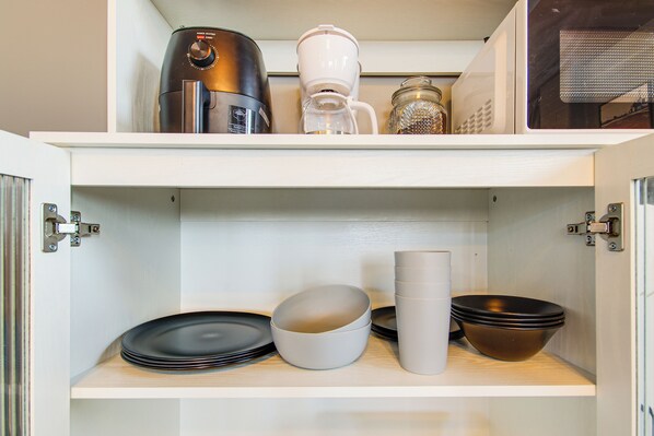 A kitchen cabinet with a coffee maker, a coffee pot, and various bowls and plates.