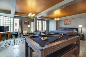 A hotel room with a pool table, a bed, a television, and a large window.