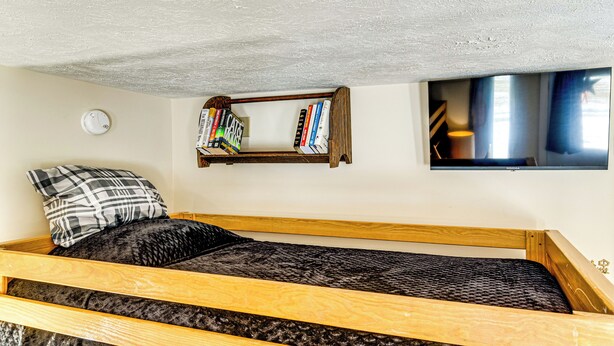 A small, cozy room with a single bed, a bookshelf, a mounted television, and a smoke detector on the wall. - Outdoorsy Delphi Retreat w/ Fishing Pond + Trails (Delphi)