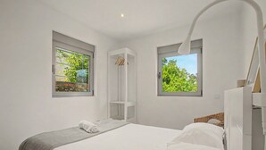 A bedroom with a bed, a wardrobe, a hanging rack, and two windows with a view of greenery. - Cantinho dos Avós – Country House with Mountain View, Wi-Fi and Air Conditioning (Sever do Vouga)
