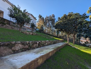 A grassy slope with a stone retaining wall, trees, and a building in the background.