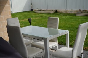 A patio with a glass-top table and four white chairs.
