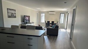Eine moderne Küche mit Kochinsel, ein Essbereich mit Tisch und Stühlen, ein Wohnzimmer mit Sofa und ein Flur, der zu einer Tür führt.