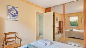 Une chambre à coucher comprenant un lit, une chaise, une armoire et une porte donnant sur une autre pièce.