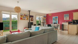 Un salon moderne avec un canapé gris, une table à manger et des chaises. On y trouve également un coin cuisine avec un meuble en bois et un mur décoré d’un motif rouge.