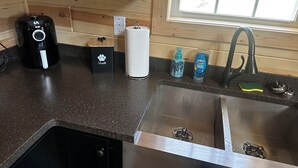 A kitchen with a coffee maker, a pet treat container, a paper towel holder, a soap dispenser, and a faucet. - Sapphire Cabin, Hot Tub, Fire Pit & Bourbon Trail, Sleeps 6 (Willisburg)