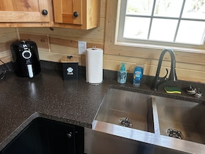 Une cuisine équipée d’une machine à café, d’un récipient pour les friandises des animaux de compagnie, d’un porte-essuie-tout, d’un distributeur de savon et d’un robinet.