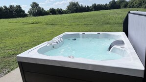 A hot tub outdoors with a grassy field and trees in the background. - Sapphire Cabin, Hot Tub, Fire Pit & Bourbon Trail, Sleeps 6 (Willisburg)