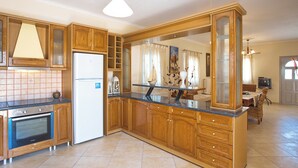 Eine Küche mit Holzausstattung, einem Kühlschrank, einem Backofen und einer Kochinsel mit Glasplatte.