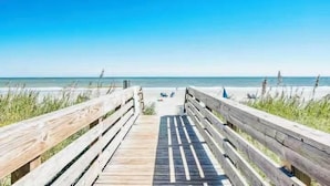 Ein hölzerner Steg führt zu einem Strand unter blauem Himmel.