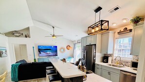 Eine moderne Küche mit Kochinsel, Barhocker, Deckenventilator und großem Fernseher.