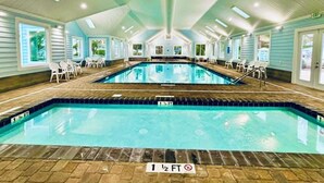 Ein Hallenbad mit klarem Wasser, umgeben von weißen Stühlen und einem gefliesten Boden.