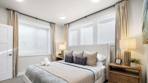 A bedroom with a large bed, two bedside tables, a nightstand, a lamp, and a clock.