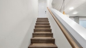 A wooden staircase with a white handrail and a woven mat at the bottom.