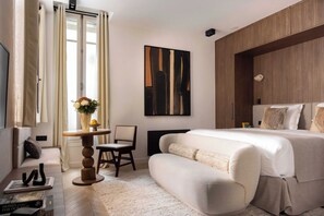 Une chambre moderne avec un grand lit, un canapé, une petite table sur laquelle est posé un vase, et un tableau accroché au mur.