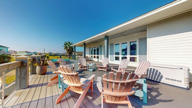 Une terrasse extérieure couverte, dotée de fauteuils Adirondack, d’un groupe électrogène Generac et offrant une vue sur la plage.