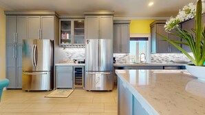 Une cuisine moderne dotée d’appareils électroménagers en acier inoxydable, d’un plan de travail en marbre et d’un mur d’accent jaune.