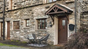 A stone building with a wooden door, two windows, and a small outdoor seating area with a table and chairs. - 1 Force Mill Barn in Satterthwaite (Ulverston)