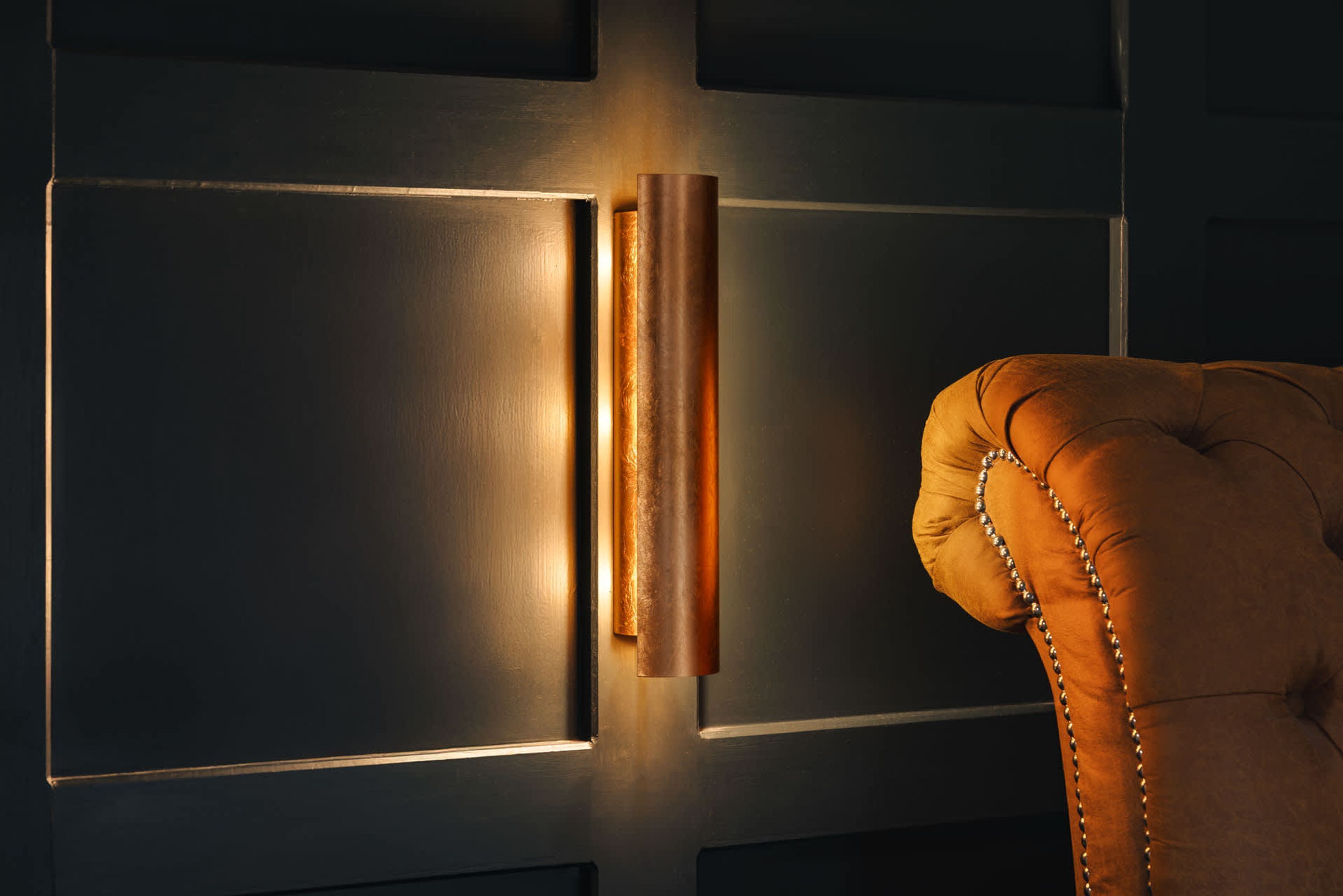 A dark room with a wall-mounted light fixture and a tufted leather armchair.