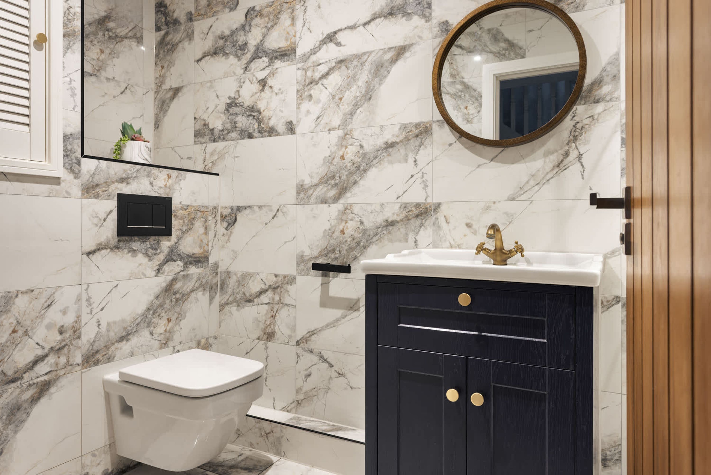 A bathroom with a toilet, a sink with a gold faucet, and a mirror with a wooden frame.
