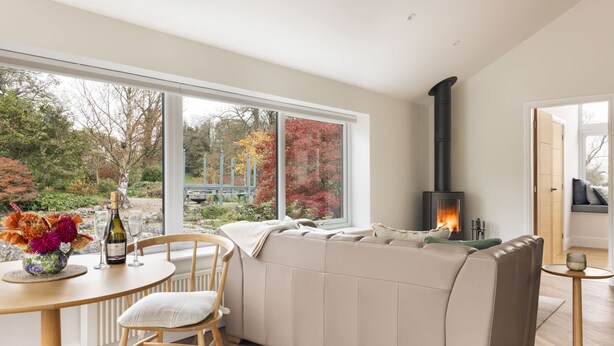 A modern living room with a large window, a sofa, a fireplace, and a dining area with a table and chairs. - The Lookout With 1 Bedrooms and 1 Bathrooms (Grange-over-Sands)