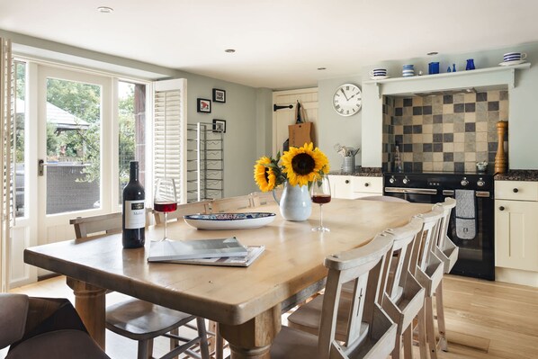 A kitchen with a wooden table, chairs, a clock, and a tiled backsplash. - Glen Bank in Brampton (Appleby-in-Westmorland)