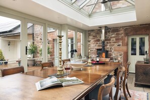 A spacious dining area with a long wooden table, chairs, and a glass ceiling. - Glen Bank in Brampton (Appleby-in-Westmorland)
