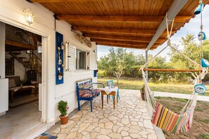 A covered patio with a stone floor, a wooden ceiling, a bench, a table, and a hammock. - Petalidi Sunny Home One - Charming Garden Nest (Messini)