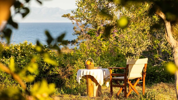 A wooden table with a white tablecloth and a wicker basket of fruit, a wooden chair, and a view of the sea. - Petalidi Sunny Home One - Charming Garden Nest (Messini)