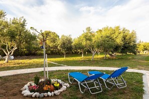 A garden area with a stone pathway, blue lounge chairs, and a small tree with a hanging ornament. - Petalidi Sunny Home One - Charming Garden Nest (Messini)