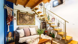 A cozy living room with a sofa, a coffee table with a plant, and a staircase with a TV mounted on the wall. - Petalidi Sunny Home One - Charming Garden Nest (Messini)