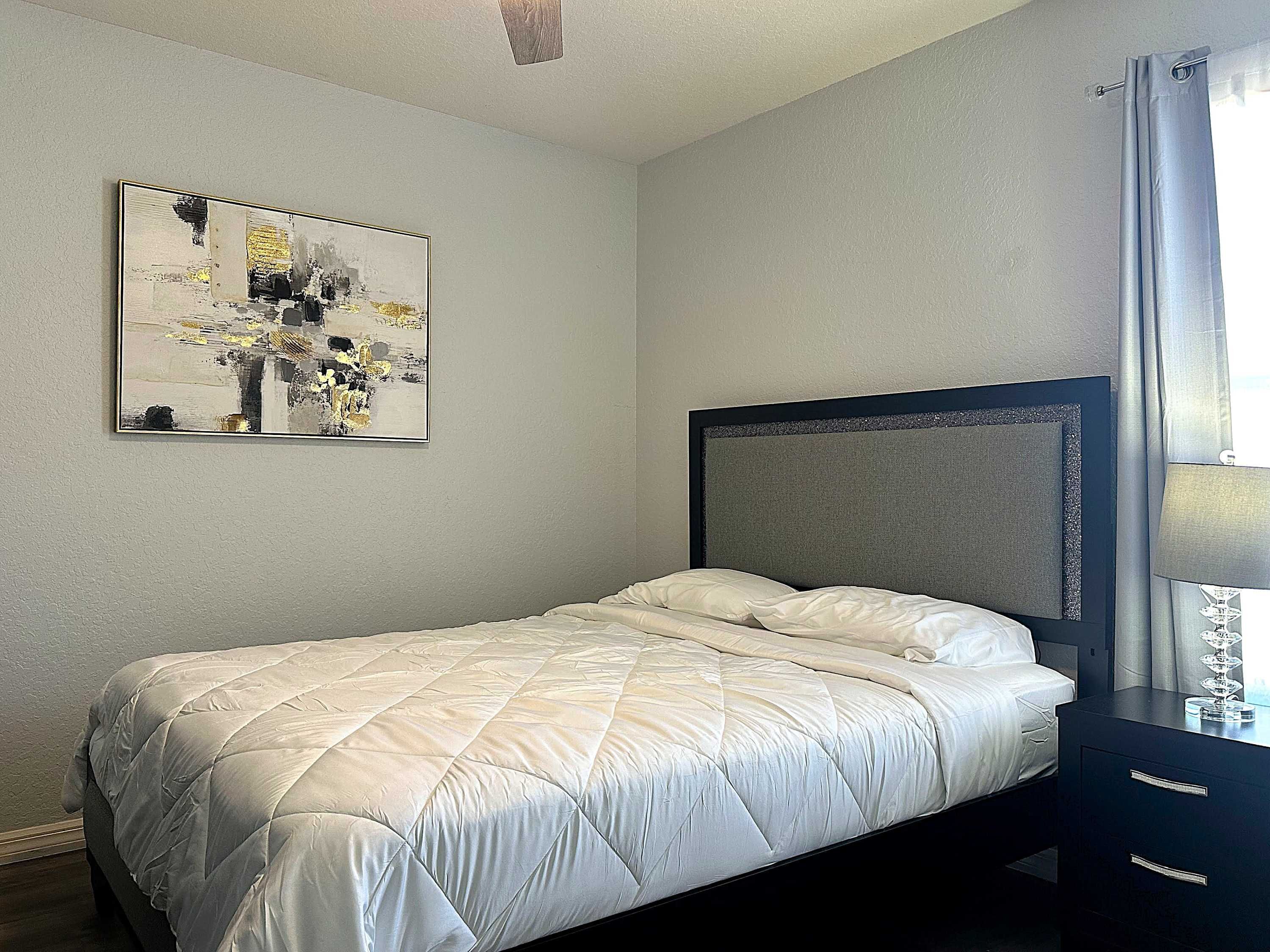 A neatly made bed with a quilted white duvet in a room with a plain wall and a ceiling light fixture.