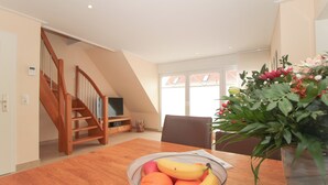 A dining area with a wooden table, a bowl of fruit, a potted plant, and a staircase leading to another room. - Exclusive vacation apartment in Norddeich, just a few minutes' walk from the sea. (Norden)