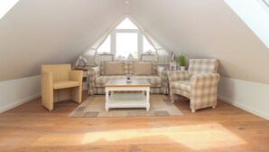 A cozy attic room with a wooden floor, a sofa, a chair, and a coffee table. - Exclusive vacation apartment in Norddeich, just a few minutes' walk from the sea. (Norden)