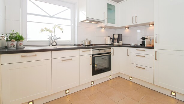 A modern kitchen with white cabinets, a built-in oven, and a window with plants. - Exclusive vacation apartment in Norddeich, just a few minutes' walk from the sea. (Norden)