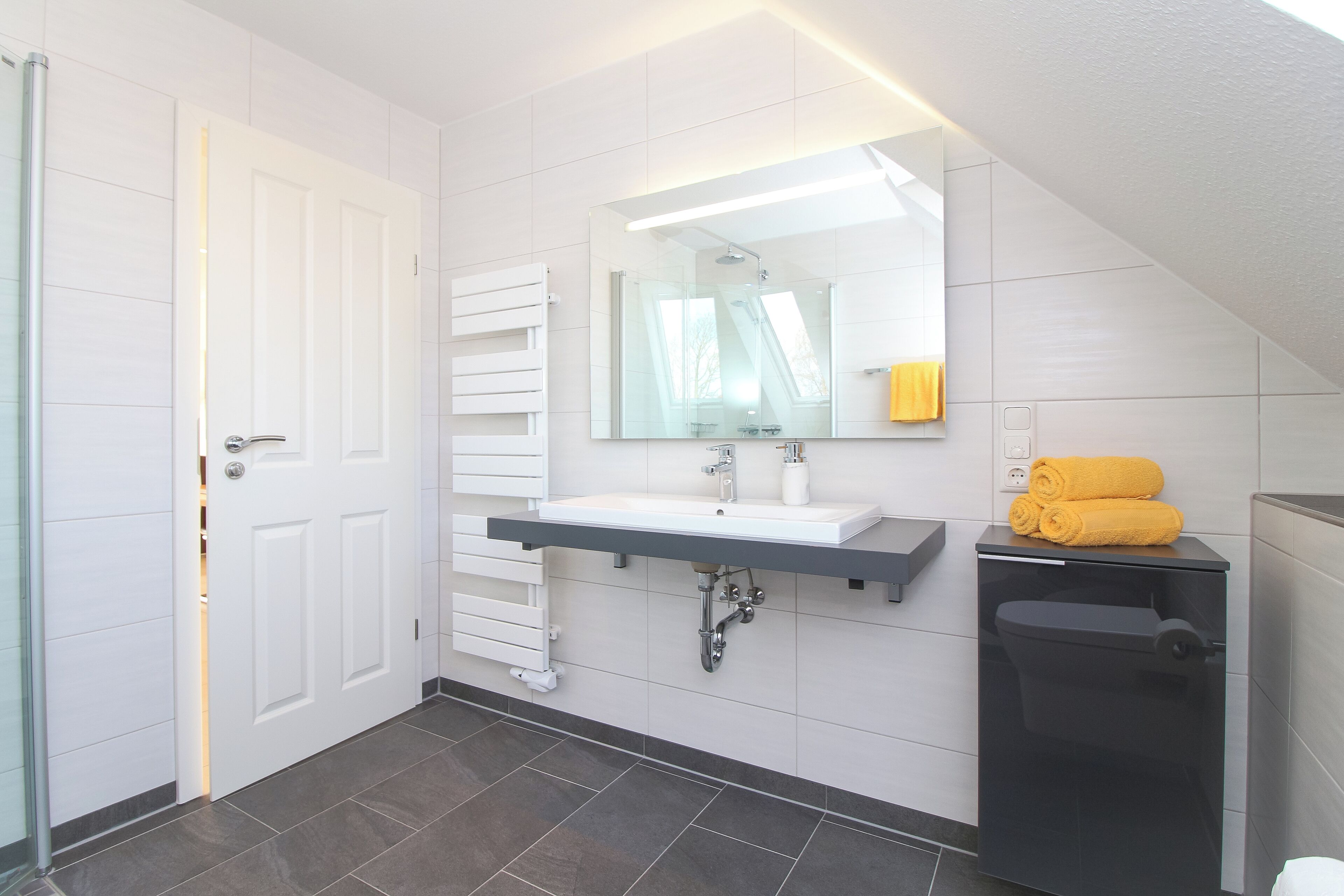 Un bagno moderno con un mobile lavabo bianco, uno specchio grande, un water nero e un portasciugamani con asciugamani gialli.